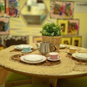 Home corner dramatic play area with round table set with tea set and plant at Innovative Early Learning